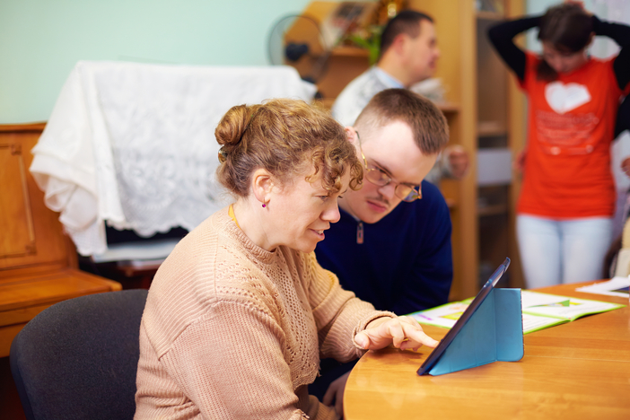 Two people with special needs sitting at the desk and looking at a tablet.